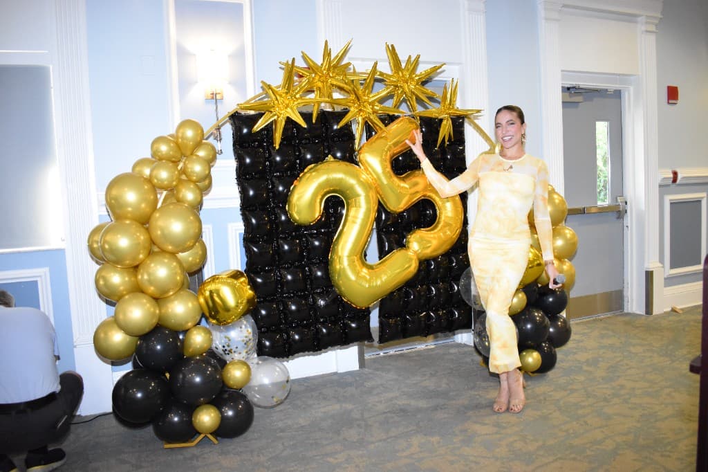 HHI leader beside the 25th anniversary balloon backdrop