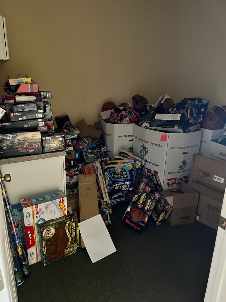 Volunteers in holiday shirts standing behind stacked Toys for Tots donation boxes