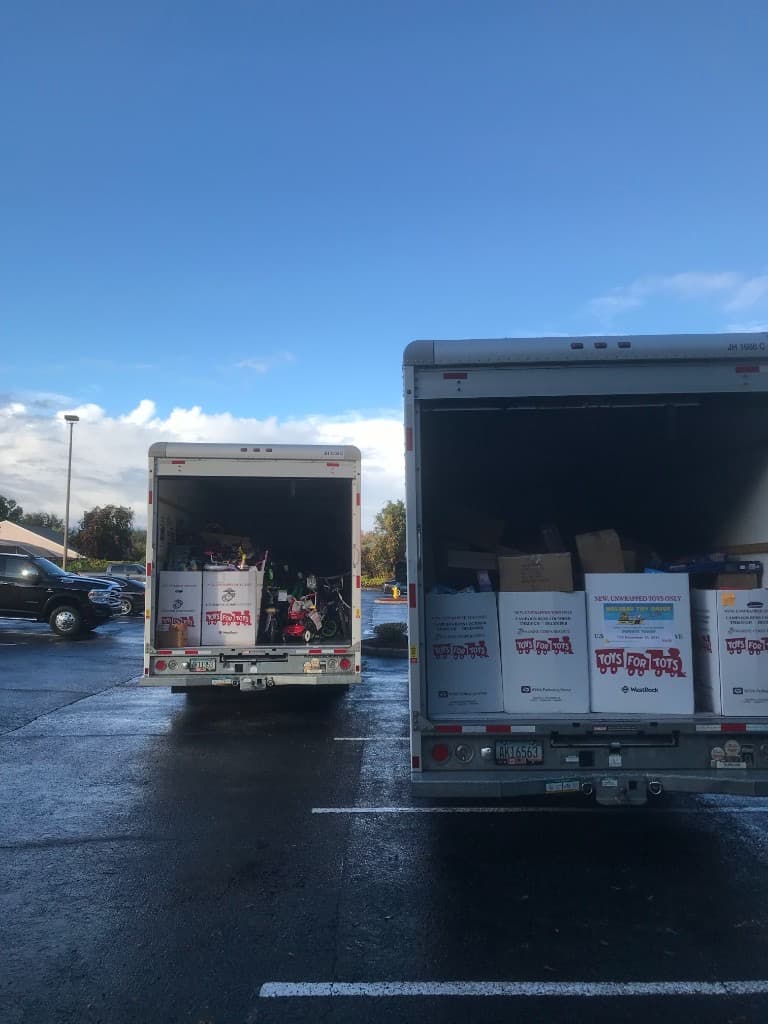 Three volunteers in holiday hats standing behind U.S. Marine Corps Reserve Toys for Tots boxes