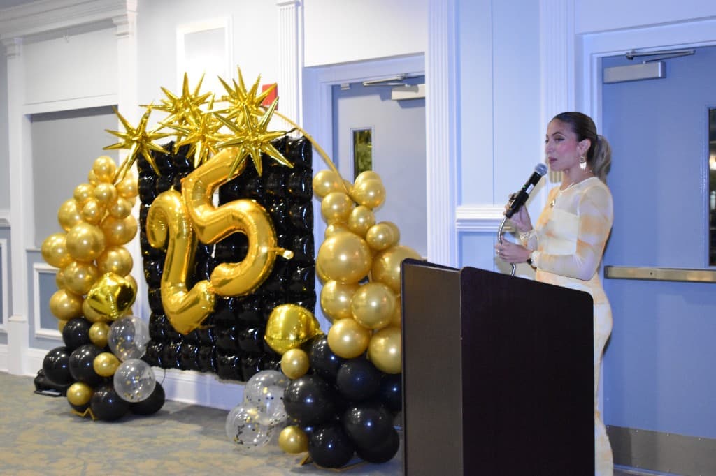 HHI leader speaking at the 25th anniversary celebration beside gold balloon display